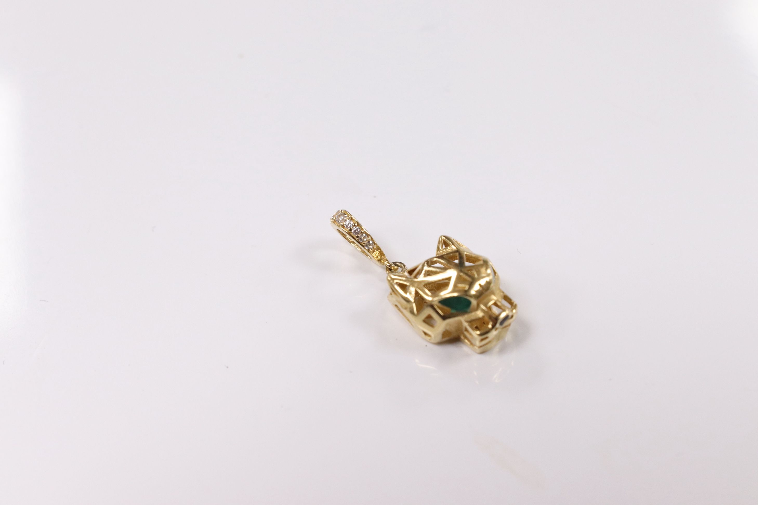 A modern Cartier style pierced 18k and emerald? set pendant, modelled as a leopard's head, with diamond chip set bale, overall 27mm, gross weight 2.5 grams. Condition - fair